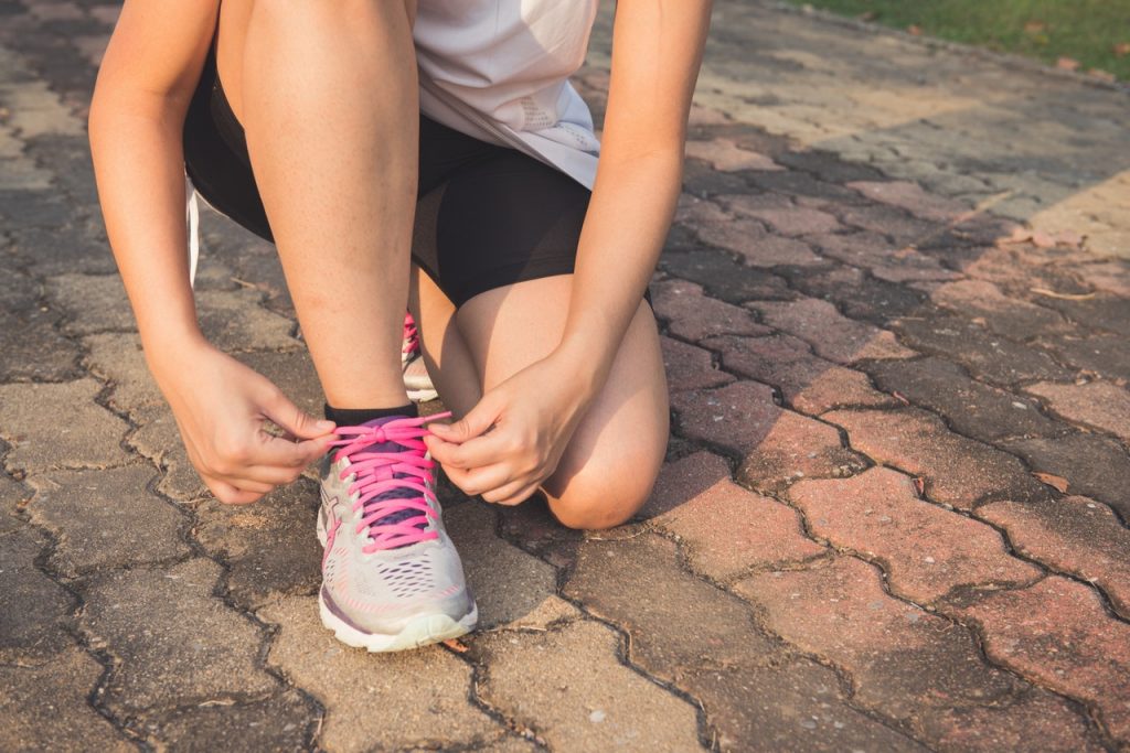 a woman lacing up her gray and pink shoe